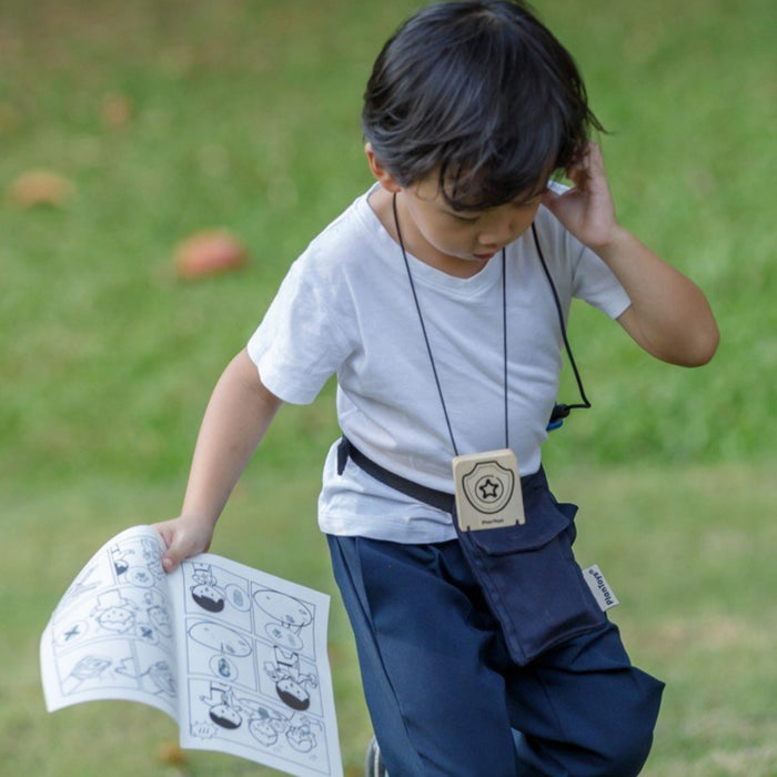 young toddler walking outside in grass on a mission, using walking talkie, wearing the badge, and carrying the spy comic